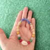 Pulseira de Contas Coloridas e Búzio - Sabedoria e Proteção de Bali: Traga a beleza serena e a sabedoria ancestral da Ilha dos Deuses, Bali (Indonésia), diretamente para o seu pulso. Esta pulseira esotérica artesanal é um poderoso amuleto de proteção e vitalidade, cuidadosamente feita à mão por mestres artesãos balineses.  Energias e Significado Espiritual: As vibrantes contas coloridas não são apenas decorativas; elas representam a energia dos diferentes Chakras, promovendo o equilíbrio energético e infundindo o seu dia com alegria, positivismo e vitalidade. O ponto focal é o búzio natural, um símbolo místico profundamente ligado à espiritualidade e ao mar: Poder Feminino: Representa a Deusa, a beleza natural e a fertilidade, fortalecendo a energia feminina (Yin). Conhecimento Antigo: Simboliza a sabedoria e o conhecimento ancestral, guiando a jornada interior. Proteção Marítima: Atua como um talismã de proteção, promovendo a fluidez e a consciência plena. Uma Joia Espiritual Essencial: Com um design intemporal e ajuste perfeito, esta pulseira unissexo é ideal para qualquer pessoa que procure um acessório esotérico que vá além da estética. É um lembrete constante da sua força interior e da busca por uma vida mais consciente e espiritualmente conectada.Detalhes do Produto: Origem: Bali, Indonésia (Artesanato Autêntico) Significado: Equilíbrio de Chakras, Proteção Espiritual, Sabedoria e Vitalidade. Uso: Joia Espiritual Unissexo (Homens e Mulheres) Vantagem: Leve e ajustável, garantindo o máximo conforto e adaptabilidade. Leve consigo a magia de Bali e a poderosa energia da sabedoria e da beleza natural.