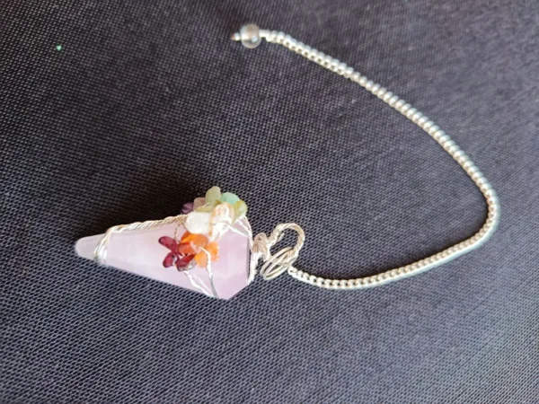 Pêndulo de Quartzo Rosa e 7 Chakras - Radiestesia, Amor e Equilíbrio Energético Eleve sua prática radiestésica e harmonize seu campo vibracional com este deslumbrante Pêndulo de Cura, uma ferramenta esotérica poderosa que combina a energia do Amor Incondicional do Quartzo Rosa com o alinhamento completo dos seus centros energéticos. 💎 A Força do Quartzo Rosa para Radiestesia Este pêndulo é meticulosamente esculpido em Quartzo Rosa natural, a pedra do amor, paz e cura emocional. Propriedades de Cura: Atua diretamente no Chakra Cardíaco, acalmando o sistema nervoso e promovendo a autoestima, a aceitação e a abertura para receber e dar amor. Vibração Ideal: Sua energia suave e compassiva é perfeita para radiestesistas que buscam sensibilidade e empatia em seus trabalhos. Aplicações Terapêuticas: Ideal para detecção de padrões energéticos em relacionamentos, localização de bloqueios emocionais e medição da vibração de ambientes para promover harmonia e bem-estar. 🌈 O Toque dos 7 Chakras: Multiplicador de Energia O pêndulo é ricamente adornado na sua corrente com pequenas pedras naturais representando os sete principais chakras. Esta adição é fundamental para potencializar sua prática de cura energética: Equilíbrio e Neutralidade: Cada pedra (representando os chakras Raiz ao Coroa) atua como um multiplicador de energia, garantindo que o instrumento de radiestesia opere a partir de um estado de equilíbrio vibracional e neutralidade completa. Foco e Precisão: Ajuda o operador a manter a conexão intuitiva com todos os seus centros de energia durante a consulta, resultando em respostas intuitivas mais claras e precisas. Adquira o Seu! Este pêndulo divinatório é um instrumento de trabalho que une a beleza da natureza à potência energética necessária para suas investigações. Perfeito para quem busca respostas intuitivas ancoradas no amor e na harmonia. Leve o equilíbrio dos chakras e a suavidade do Quartzo Rosa para a sua mesa de trabalho esotérica!