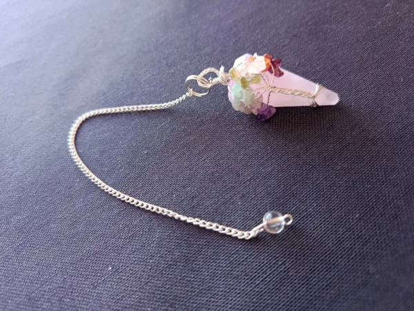 Pêndulo de Quartzo Rosa e 7 Chakras - Radiestesia, Amor e Equilíbrio Energético Eleve sua prática radiestésica e harmonize seu campo vibracional com este deslumbrante Pêndulo de Cura, uma ferramenta esotérica poderosa que combina a energia do Amor Incondicional do Quartzo Rosa com o alinhamento completo dos seus centros energéticos. 💎 A Força do Quartzo Rosa para Radiestesia Este pêndulo é meticulosamente esculpido em Quartzo Rosa natural, a pedra do amor, paz e cura emocional. Propriedades de Cura: Atua diretamente no Chakra Cardíaco, acalmando o sistema nervoso e promovendo a autoestima, a aceitação e a abertura para receber e dar amor. Vibração Ideal: Sua energia suave e compassiva é perfeita para radiestesistas que buscam sensibilidade e empatia em seus trabalhos. Aplicações Terapêuticas: Ideal para detecção de padrões energéticos em relacionamentos, localização de bloqueios emocionais e medição da vibração de ambientes para promover harmonia e bem-estar. 🌈 O Toque dos 7 Chakras: Multiplicador de Energia O pêndulo é ricamente adornado na sua corrente com pequenas pedras naturais representando os sete principais chakras. Esta adição é fundamental para potencializar sua prática de cura energética: Equilíbrio e Neutralidade: Cada pedra (representando os chakras Raiz ao Coroa) atua como um multiplicador de energia, garantindo que o instrumento de radiestesia opere a partir de um estado de equilíbrio vibracional e neutralidade completa. Foco e Precisão: Ajuda o operador a manter a conexão intuitiva com todos os seus centros de energia durante a consulta, resultando em respostas intuitivas mais claras e precisas. Adquira o Seu! Este pêndulo divinatório é um instrumento de trabalho que une a beleza da natureza à potência energética necessária para suas investigações. Perfeito para quem busca respostas intuitivas ancoradas no amor e na harmonia. Leve o equilíbrio dos chakras e a suavidade do Quartzo Rosa para a sua mesa de trabalho esotérica!