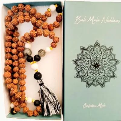 Colar Mala de Bali Artesanal  | Confiança | Feito à Mão Apresentamos um autêntico Colar Mala de Bali, uma peça de artesanato que transcende a simples beleza. Este colar, tradicionalmente conhecido como Japa Mala, é mais do que um acessório étnico; é um poderoso amuleto de confiança e uma ferramenta ancestral para qualquer prática de meditação, yoga na entoação das Mantras e mindfulness. Cada Mala contém as místicas 108 contas, um número que simboliza a totalidade da vida e a conexão entre o corpo, a mente e o espírito. O Mala da Confiança representa os cinco elementos clássicos: Terra (Prithvi/Bhumi), com estabilidade e conexão com as raízes. Água (Jala/Varuna) com fluidez, emoções e intuição. Fogo (Agni/Tejas) – com energia, transformação e força interior. Ar (Vayu/Pavan) com movimento, liberdade e clareza mental. Éter (Akasha) com espiritualidade, expansão e conexão universaAcredita-se que a harmonização destas energias contribui para um equilíbrio físico, mental e espiritual, promovendo confiança e bem-estar. Significado e Propósito (Confiança): O uso de um colar Mala ajuda a focar a mente e a intenção. Ao deslizar os dedos por cada uma das [Normalmente 108] contas, pode recitar um mantra ou afirmação. Este colar específico foi concebido para fortalecer a confiança e a determinação, servindo como um lembrete físico do seu poder interior e resiliência. Especificações Principais: Autenticidade Balinesa: Produto genuíno de artesanato da Indonésia, refletindo a tradição espiritual local. Feito à Mão: Cada nó e cada montagem são realizados manualmente com precisão e cuidado, garantindo durabilidade e uma textura tátil agradável. Design Boho-Chic: Combina a funcionalidade espiritual com um estilo boho e zen, perfeito para uso diário como um colar longo ou enrolado no pulso como pulseira. Amuletos e Talismãs: Um acessório carregado de significado, ideal para quem valoriza joalharia com propósito e acessórios artesanais.Ideal Para: Praticantes de meditação e yoga. Quem procura um acessório simbólico para aumentar a confiança e a clareza mental. Amantes de decoração étnica e estilo natural. Presentes originais e cheias de significado! Detalhes do Produto: Nome do Produto: Colar Mala de Bali - Confiança Origem: Bali, Indonésia Nota: As propriedades metafísicas atribuídas às pedras ou sementes são baseadas em crenças culturais e práticas espirituais. Cada Mala é único, podendo haver ligeiras variações de cor e tamanho.