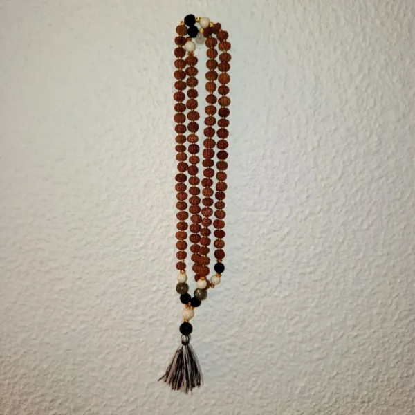 Colar Mala de Bali Artesanal  | Confiança | Feito à Mão Apresentamos um autêntico Colar Mala de Bali, uma peça de artesanato que transcende a simples beleza. Este colar, tradicionalmente conhecido como Japa Mala, é mais do que um acessório étnico; é um poderoso amuleto de confiança e uma ferramenta ancestral para qualquer prática de meditação, yoga na entoação das Mantras e mindfulness. Cada Mala contém as místicas 108 contas, um número que simboliza a totalidade da vida e a conexão entre o corpo, a mente e o espírito. O Mala da Confiança representa os cinco elementos clássicos: Terra (Prithvi/Bhumi), com estabilidade e conexão com as raízes. Água (Jala/Varuna) com fluidez, emoções e intuição. Fogo (Agni/Tejas) – com energia, transformação e força interior. Ar (Vayu/Pavan) com movimento, liberdade e clareza mental. Éter (Akasha) com espiritualidade, expansão e conexão universaAcredita-se que a harmonização destas energias contribui para um equilíbrio físico, mental e espiritual, promovendo confiança e bem-estar. Significado e Propósito (Confiança): O uso de um colar Mala ajuda a focar a mente e a intenção. Ao deslizar os dedos por cada uma das [Normalmente 108] contas, pode recitar um mantra ou afirmação. Este colar específico foi concebido para fortalecer a confiança e a determinação, servindo como um lembrete físico do seu poder interior e resiliência. Especificações Principais: Autenticidade Balinesa: Produto genuíno de artesanato da Indonésia, refletindo a tradição espiritual local. Feito à Mão: Cada nó e cada montagem são realizados manualmente com precisão e cuidado, garantindo durabilidade e uma textura tátil agradável. Design Boho-Chic: Combina a funcionalidade espiritual com um estilo boho e zen, perfeito para uso diário como um colar longo ou enrolado no pulso como pulseira. Amuletos e Talismãs: Um acessório carregado de significado, ideal para quem valoriza joalharia com propósito e acessórios artesanais.Ideal Para: Praticantes de meditação e yoga. Quem procura um acessório simbólico para aumentar a confiança e a clareza mental. Amantes de decoração étnica e estilo natural. Presentes originais e cheias de significado! Detalhes do Produto: Nome do Produto: Colar Mala de Bali - Confiança Origem: Bali, Indonésia Nota: As propriedades metafísicas atribuídas às pedras ou sementes são baseadas em crenças culturais e práticas espirituais. Cada Mala é único, podendo haver ligeiras variações de cor e tamanho.