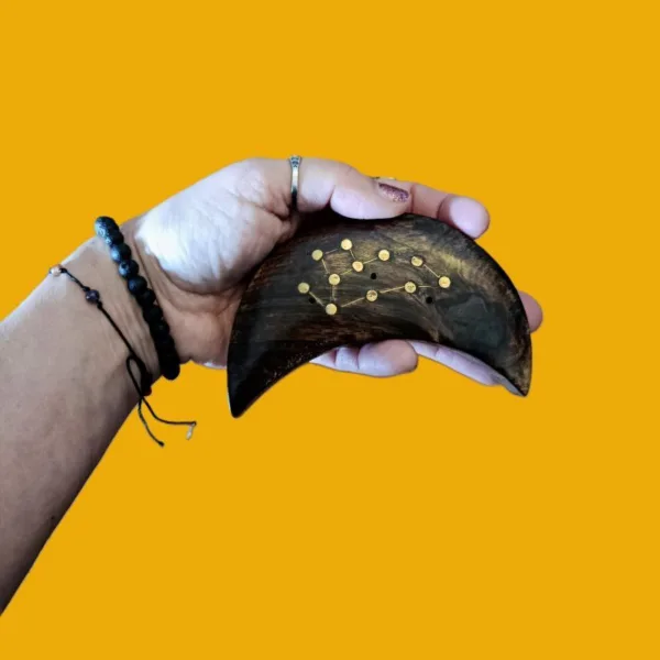 Suporte de Incenso em Madeira Meia-Lua: Constelação de Peixes (Artesanato da Índia)Transforme o seu ritual de defumação numa experiência celestial. O nosso Suporte de Incenso em Madeira em forma de Meia-Lua é mais do que um acessório; é uma peça de arte mística, esculpida à mão por artesãos talentosos na Índia, capturando a essência espiritual do signo de Peixes.A Magia Diferenciadora dos Detalhes: Constelação Incrustada em latãoO grande diferencial deste artesanato reside na sua incrustação metálica detalhada, que desenha com precisão a Constelação de Peixes.Madeira de Manga - Alta Qualidade: Feito em madeira de Manga, durável com acabamento rústico e natural, que traz o elemento "Terra" para o seu altar ou seu espaço de meditação ou de práticas de Autocuidado e AutoAmor!Simbologia Esotérica: A união da Lua (emoções e subconsciente) com a constelação de Peixes (espiritualidade e sonhos) cria um amuleto poderoso para si! Um autêntico artesanato Ativador da sua Transformação Energética!Para quê usar este Suporte de Incensos da lojaom.pt?Se é um nativo de Peixes, ou se deseja invocar as energias de serenidade, sensibilidade e intuição deste signo, este suporte é indispensável. É o artigo ideal para:Rituais de Meditação: Queime o seu incenso favorito enquanto se conecta com as estrelas. Até pode queimar 3 incensos em simultâneo, neste suporte.Decoração Esotérica: Uma peça que se destaca em qualquer prateleira, mesa, num espaço de ioga, meditação e/ou práticas energéticas.Presente com Significado: Surpreenda alguém especial com um  artesanato indiano autêntico que celebra a sua identidade astrológica! O Presente Perfeito para a Temporada de PeixesNão se contente com o comum, cada suporte é único! Traga para o seu lar um pedaço do céu noturno e a tradição milenar da Índia, num artesanato feito segundo tradições ancestrais. Este suporte de incenso é o companheiro perfeito para os nossos Óleos de Fragrância do Zodíaco, criando uma sinergia completa de aroma e simbolismo.Compre o seu suporte meia-lua - signo de Peixes hoje mesmo!