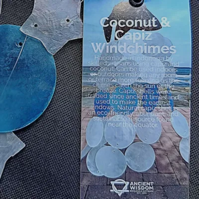 Sino de Vento|Coco e Capiz: Estrelas Brancas e Círculos Azuis – Harmonia e Brisa Celestial Leve a melodia suave do oceano e a luz das estrelas para o seu Lar! O Sino de Vento feito de Coco e Capiz (proveniente de conchas), com o seu design encantador de estrelas brancas e círculos azuis, é a peça de artesanato perfeita para quem procura equilibrar as energias do ambiente com beleza e serenidade. A Beleza das Conchas Capiz e do Elemento Ar As conchas de Capiz (também conhecidas como madrepérola translúcida) são famosas pela sua delicadeza e pelo som cristalino que produzem ao tocar umas nas outras. Combinadas com a base natural de casca de coco em forma de estrela, este mensageiro do vento une os elementos Terra e Ar: Som Terapêutico: O tilintar suave ajuda a relaxar a mente, sendo ideal para espaços de meditação, yoga, terapias energéticas e/ou varandas/terraços. Símbolo das Estrelas: No esoterismo, a estrela representa a guia espiritual, a esperança e a luz na escuridão. As cores azul e branco evocam a paz, a pureza e a proteção do céu. Cura pelo Feng Shui: Os sinos de vento são ferramentas essenciais no Feng Shui para dissipar energias estagnadas (Chi negativo) e atrair fluxo vital positivo para a entrada do seu Lar. Artesanato Sustentável e Decorativo Cada peça é única, criada por artesãos na Indonésia, feita de casca do coco em forma de estrela de 5 pontas e a textura orgânica das conchas. Este não é apenas uma peça decorativa, é um artigo de artesanato que respeita a natureza: Decoração Versátil: Fica perfeito tanto em interiores (perto de janelas) como em áreas exteriores cobertas, criando um ponto focal de luz, som e cor. Cromoterapia: O azul suave promove a comunicação e a calma, enquanto o branco limpa a vibração do espaço. Presente com Intenção: Um presente maravilhoso para quem se mudou para uma casa nova ou precisa de um toque de tranquilidade no seu dia a dia. Especificações do Produto Materiais: Casca de coco natural e conchas Capiz genuínas. Design: Estrelas em tons de Azul e Branco. Uso: Interior e Exterior (protegido da chuva direta). Vibração: Paz, Guia Espiritual e Fluidez. ✨ Deixe a Energia Fluir no Seu Lar Preencha o seu lar com a melodia das estrelas e a proteção do mar. O Sino de Vento de Coco e Capiz é "aquele" toque especial que o seu lar merece. Dica Ativadora: Pendure o seu sino de vento perto de uma janela, ou da porta da sua varanda ou quintal para filtrar as energias que entram para dentro do seu Lar! Comprar Sino de Vento Estrelas – Traga a Harmonia para Casa