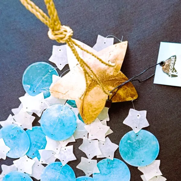 Sino de Vento|Coco e Capiz: Estrelas Brancas e Círculos Azuis – Harmonia e Brisa Celestial Leve a melodia suave do oceano e a luz das estrelas para o seu Lar! O Sino de Vento feito de Coco e Capiz (proveniente de conchas), com o seu design encantador de estrelas brancas e círculos azuis, é a peça de artesanato perfeita para quem procura equilibrar as energias do ambiente com beleza e serenidade. A Beleza das Conchas Capiz e do Elemento Ar As conchas de Capiz (também conhecidas como madrepérola translúcida) são famosas pela sua delicadeza e pelo som cristalino que produzem ao tocar umas nas outras. Combinadas com a base natural de casca de coco em forma de estrela, este mensageiro do vento une os elementos Terra e Ar: Som Terapêutico: O tilintar suave ajuda a relaxar a mente, sendo ideal para espaços de meditação, yoga, terapias energéticas e/ou varandas/terraços. Símbolo das Estrelas: No esoterismo, a estrela representa a guia espiritual, a esperança e a luz na escuridão. As cores azul e branco evocam a paz, a pureza e a proteção do céu. Cura pelo Feng Shui: Os sinos de vento são ferramentas essenciais no Feng Shui para dissipar energias estagnadas (Chi negativo) e atrair fluxo vital positivo para a entrada do seu Lar. Artesanato Sustentável e Decorativo Cada peça é única, criada por artesãos na Indonésia, feita de casca do coco em forma de estrela de 5 pontas e a textura orgânica das conchas. Este não é apenas uma peça decorativa, é um artigo de artesanato que respeita a natureza: Decoração Versátil: Fica perfeito tanto em interiores (perto de janelas) como em áreas exteriores cobertas, criando um ponto focal de luz, som e cor. Cromoterapia: O azul suave promove a comunicação e a calma, enquanto o branco limpa a vibração do espaço. Presente com Intenção: Um presente maravilhoso para quem se mudou para uma casa nova ou precisa de um toque de tranquilidade no seu dia a dia. Especificações do Produto Materiais: Casca de coco natural e conchas Capiz genuínas. Design: Estrelas em tons de Azul e Branco. Uso: Interior e Exterior (protegido da chuva direta). Vibração: Paz, Guia Espiritual e Fluidez. ✨ Deixe a Energia Fluir no Seu Lar Preencha o seu lar com a melodia das estrelas e a proteção do mar. O Sino de Vento de Coco e Capiz é "aquele" toque especial que o seu lar merece. Dica Ativadora: Pendure o seu sino de vento perto de uma janela, ou da porta da sua varanda ou quintal para filtrar as energias que entram para dentro do seu Lar! Comprar Sino de Vento Estrelas – Traga a Harmonia para Casa